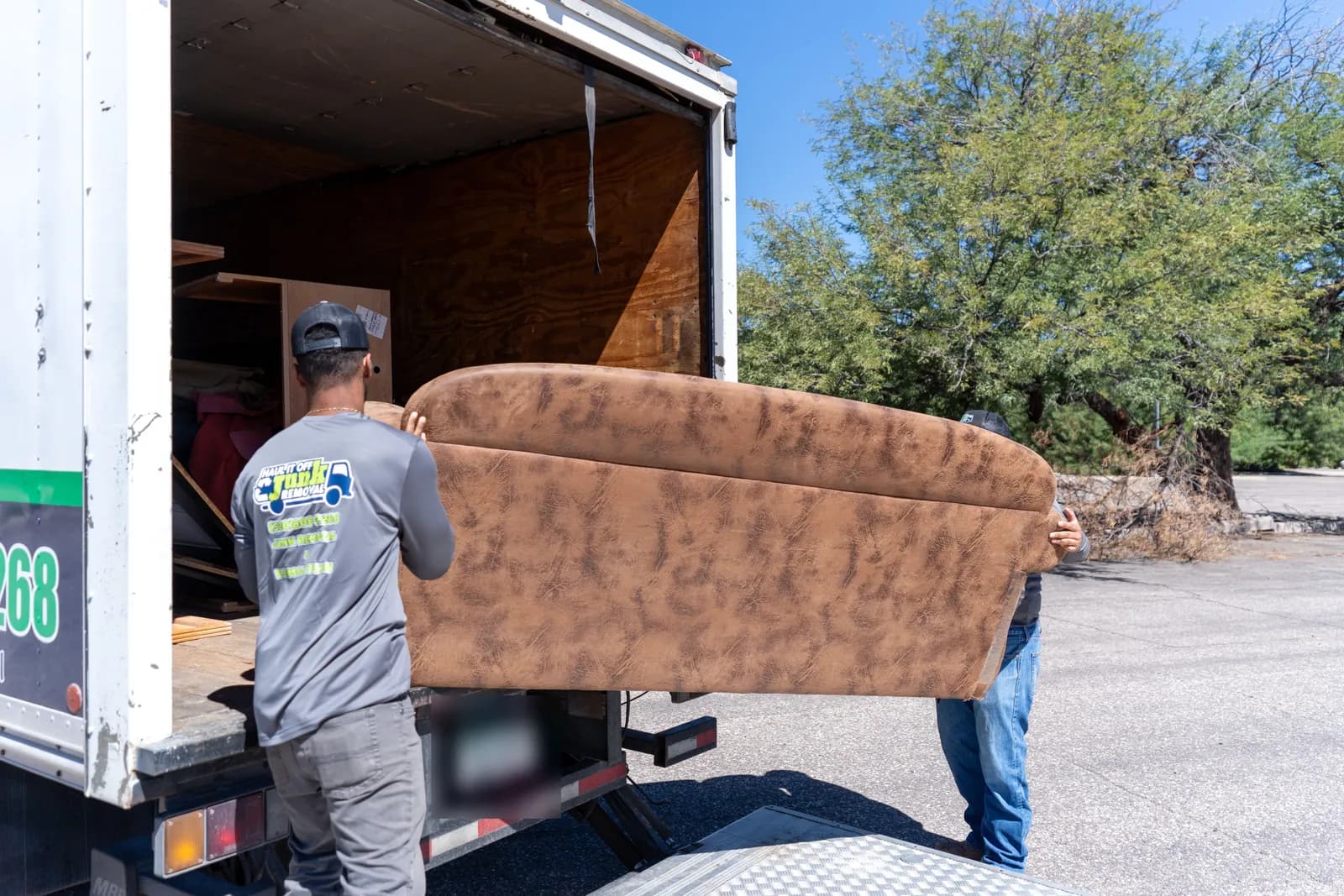 Two crew members carrying a brown couch into the back of the box truck