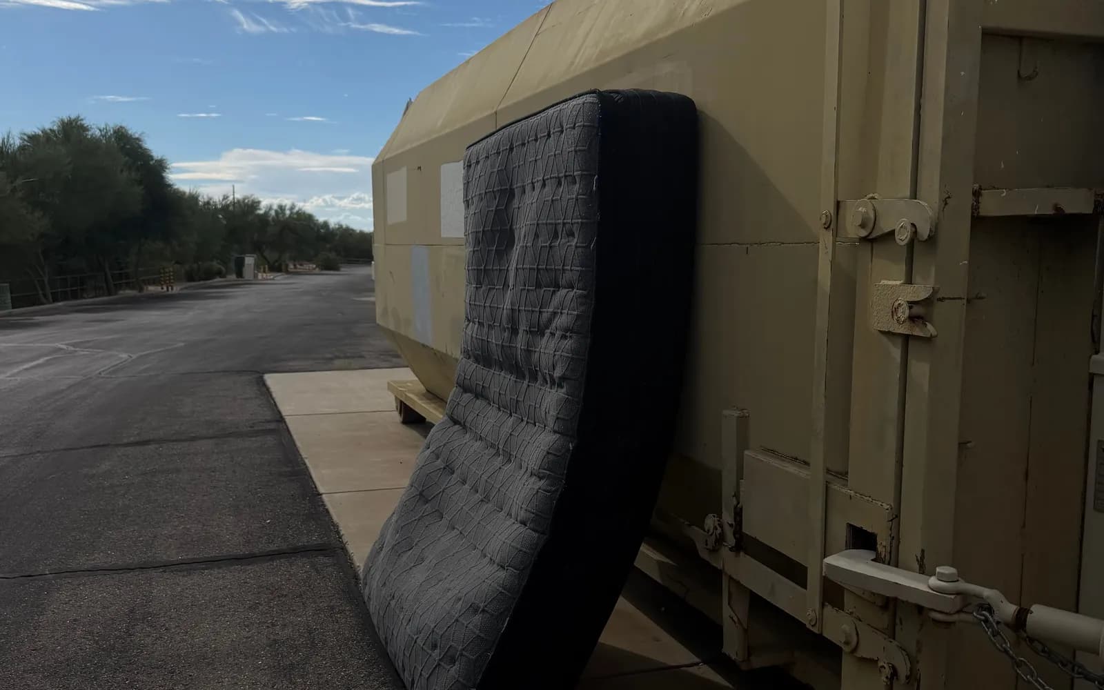 An old mattress leaning against a large metal compactor container