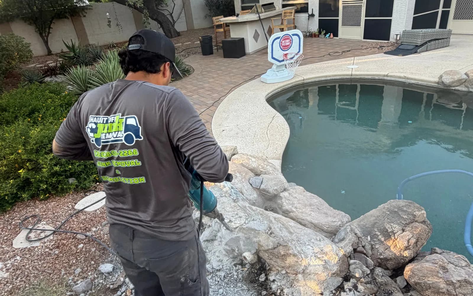 Crew member breaking up a rock pool feature with a jackhammer in a Tucson backyard